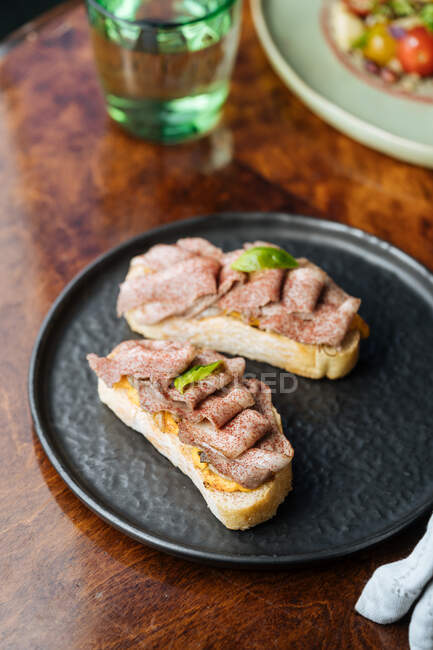 From above juicy tasty ham in row on crispy toasts on black plate on wooden table in restaurant — Stock Photo