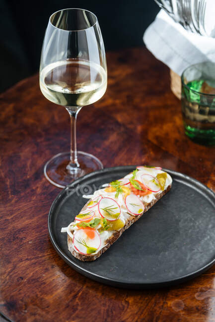 Sandwichs colorés décorés d'en haut avec des tranches de radis rouge et des herbes en sauce blanche avec du vin sur la table — Photo de stock