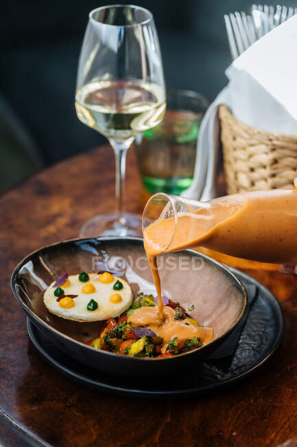 De cima prato apetitoso com mistura de vegetais coloridos e omelete derramando por molho por pessoa de cultura no restaurante — Fotografia de Stock