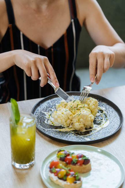 Crop woman coupe chou-fleur en sauce à table avec sandwichs et limonade fraîche au restaurant — Photo de stock