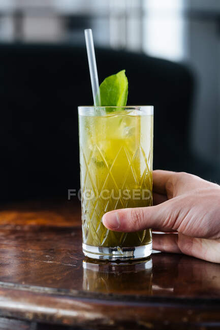 Mão o cortada pessoa irreconhecível bebendo saborosa limonada gelada com hortelã e palha na mesa à luz do sol — Fotografia de Stock