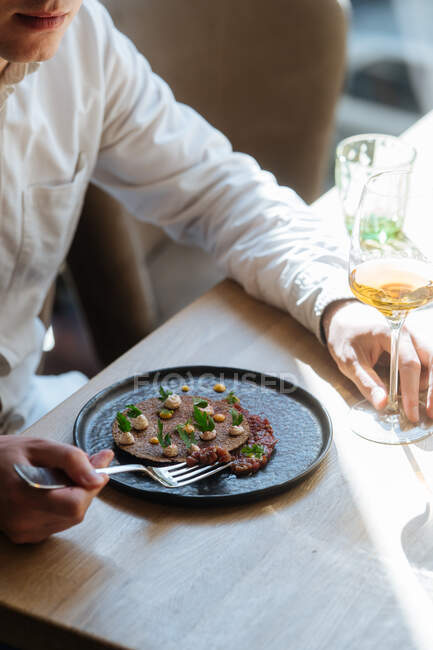 Из выше урожая человек ест вкусную овсянку, украшенную травами и горохом на тарелке подается с вином за столом — стоковое фото