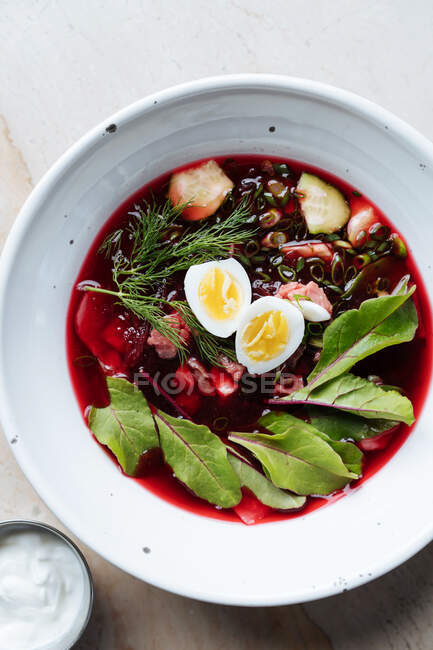 Du haut de la soupe de betteraves rouges appétissante avec des œufs durs et des herbes dans une assiette blanche sur la table — Photo de stock