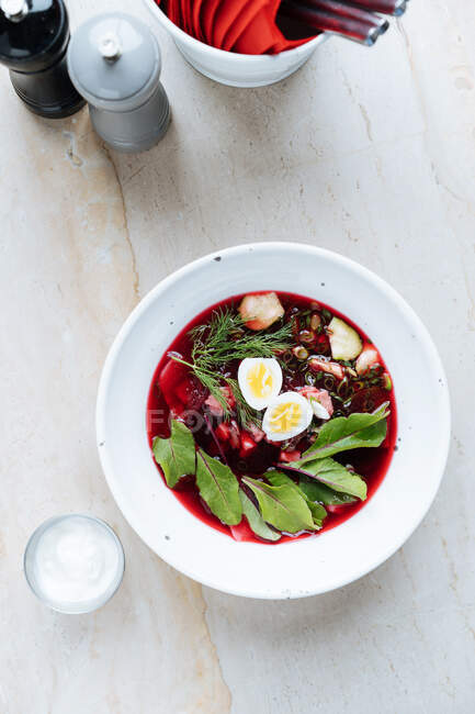From above palatable red beetroot soup with boiled eggs and herbs in white plate on table — Stock Photo