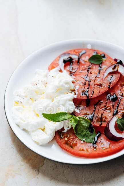 From above ripe red sliced tomatoes with red onion sour cream and herbs in plate on table — Stock Photo