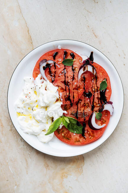 De arriba los tomates maduros rojos en rodajas con la crema agria de cebolla roja y las hierbas en el plato a la mesa - foto de stock