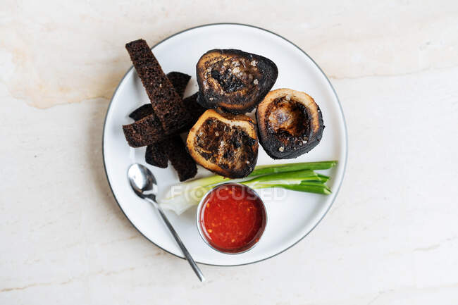 Top view of smoked rounded slices of eggplant on white plate with red sauce green onion and fried croutons of rye bread in restaurant — Stock Photo