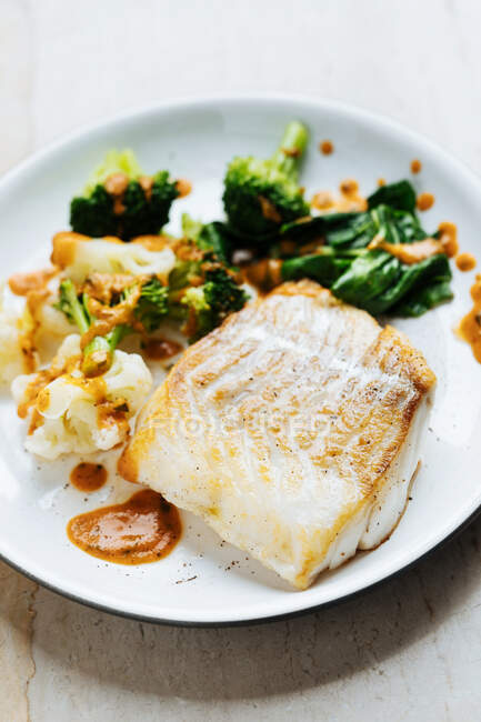 Апетитна свіжа риба з зеленню та брокколі, посипана червоним соусом на білій тарілці — стокове фото