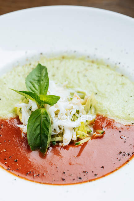 Desde arriba de sopa de crema de tomate y sopa de crema con queso en un tazón blanco decorado con rodajas de verduras y hojas de albahaca - foto de stock