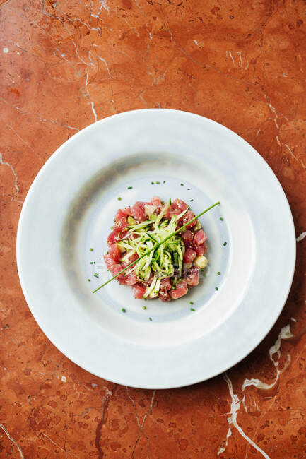 Vista superior de prato branco cerâmico com fatias de atum vermelho e queijo decorado com pedaços de pepino e especiarias no restaurante — Fotografia de Stock