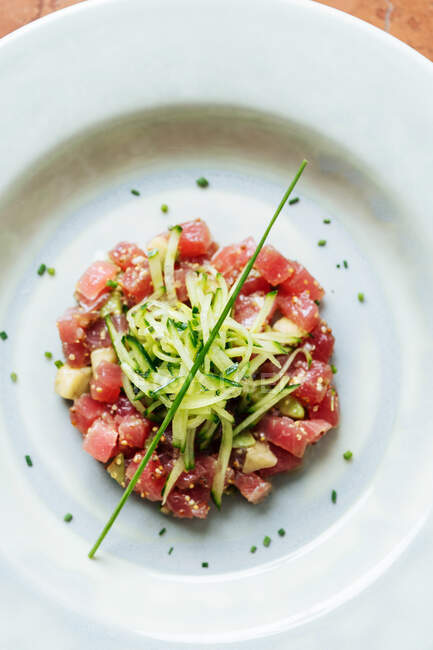 Vista dall'alto di pezzi quadrati di tonno rosso serviti con fette di cetriolo ed erbe aromatiche su piatto bianco nel ristorante — Foto stock