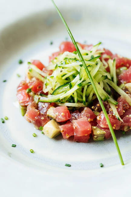 Top view of square pieces of red tuna served with slices of cucumber and herbs on white plate in restaurant — Stock Photo