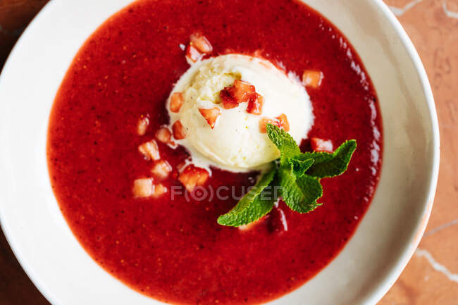 Top view of scoop of vanilla ice cream on plate with red syrup decorated with small pieces of strawberry and fresh green mint in restaurant — Stock Photo
