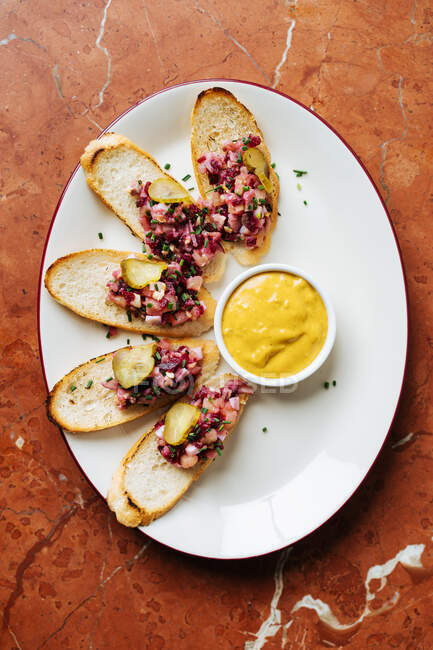 Draufsicht auf geröstete Brotscheiben mit buntem Salat und abgerundeten Salatgurkenstücken auf ovalem weißem Teller mit gelber Sauce — Stockfoto