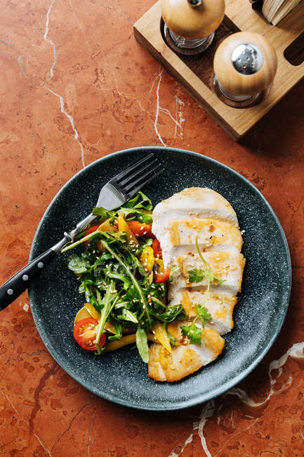 Top view of cut chicken fillet on plate with fresh salad of cherry tomatoes and herbs in restaurant — Stock Photo