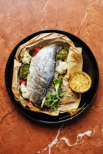 Vista superior de assado em peixe de papel com brócolis couve-flor ervas e pedaço de limão na mesa no restaurante — Fotografia de Stock