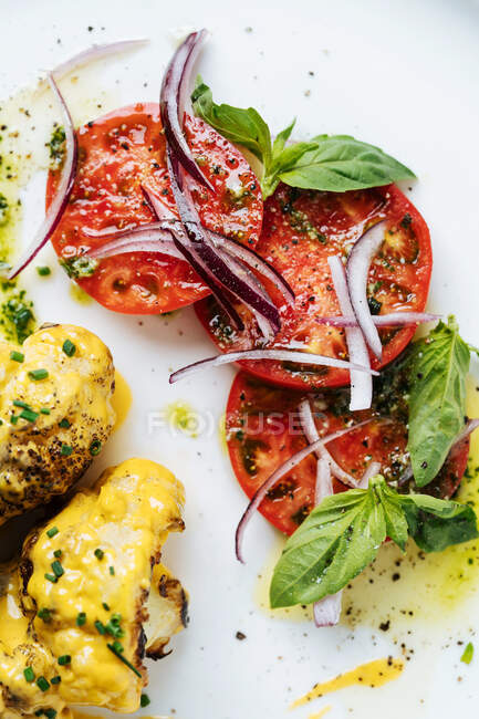 Draufsicht auf abgerundete Fleischstücke in gelber Sauce und Kräuter auf weißem Teller mit Tomatenminzscheiben und roten Zwiebeln im Restaurant — Stockfoto