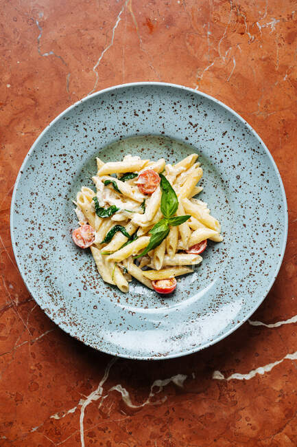 Vista superior de un plato elegante con deliciosas piezas de pasta de tomates cherry y vegetación en el restaurante - foto de stock