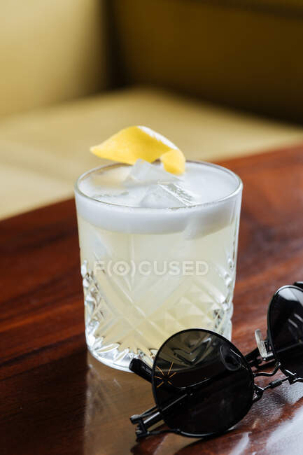 From above of alcohol cocktail with foam in stylish glass decorated with lemon zest on table neat sunglasses in restaurant — Stock Photo
