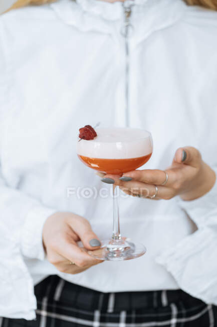 Анонімний офіціант у білій сорочці тримає смачний червоний коктейль у стильному склі, прикрашеному свіжою малиною — стокове фото