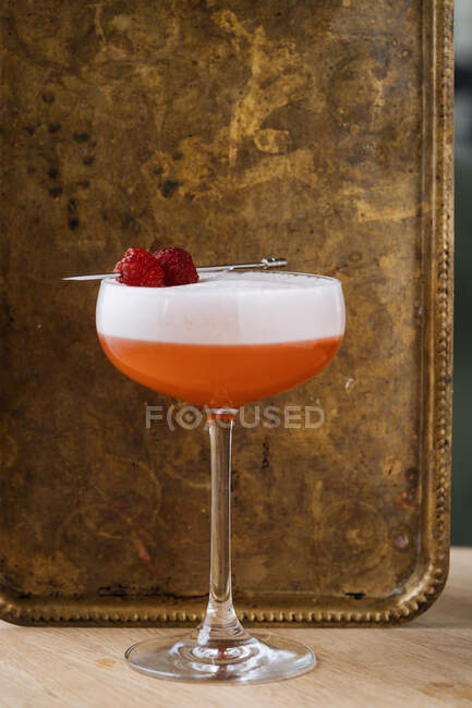 Красочный коктейль из красного спирта в стильном стакане на столе с барной ложкой и фильтром в ресторане — стоковое фото