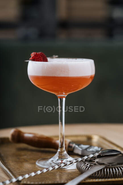 Colorful red alcohol cocktail in stylish glass on table with bar spoon and strainer in restaurant — Stock Photo