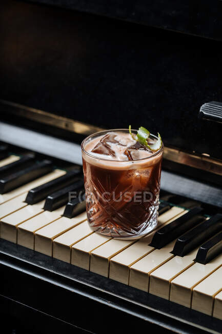 Стакан коктейля со льдом, лежащий на клавишах пианино — стоковое фото