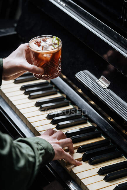 Зверху безликий чоловік грає на піаніно з однією і тримає склянку з коктейлем i іншою рукою — стокове фото