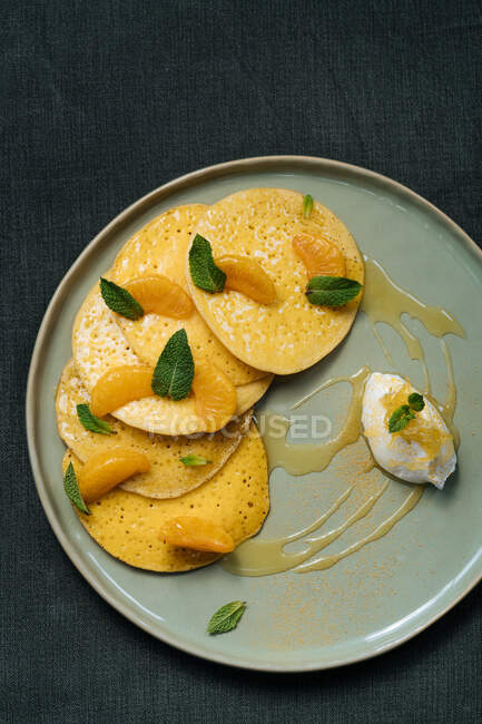From above of plate with pancakes decorated with slices of tangerine leaves of mint served with sauce and glass of orange juice — Stock Photo