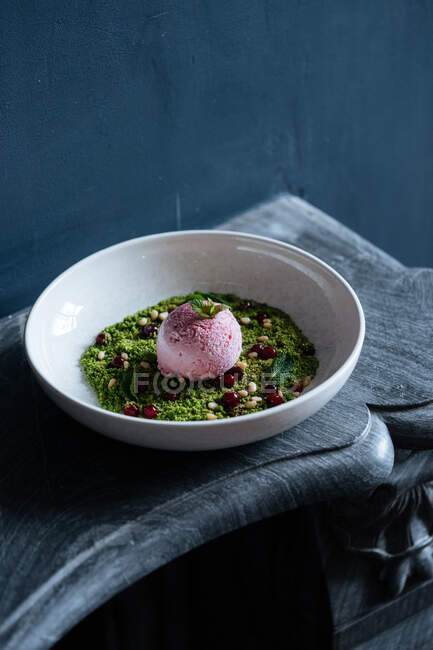 From above of scoop of purple ice cream on green mousse decorated with nuts and fresh mint in white bowl — Stock Photo