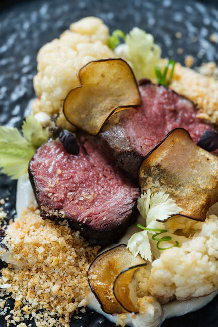Back plate with roast beef slices on creamy sauce with cauliflower and fried chips having dinner with glass of red wine — Stock Photo