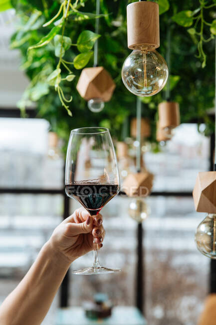 De dessous de la main féminine de la récolte avec un verre élégant de vin rouge avec l'intérieur moderne du restaurant — Photo de stock