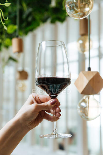 De baixo da mão feminina de colheita com vidro elegante de vinho tinto com interior moderno de restaurante — Fotografia de Stock