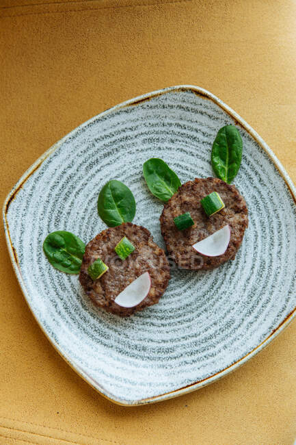 Vista superior de pequeñas chuletas con hojas de albahaca trozos de ralladura de lima y cebolla en forma de cara divertida en el restaurante - foto de stock