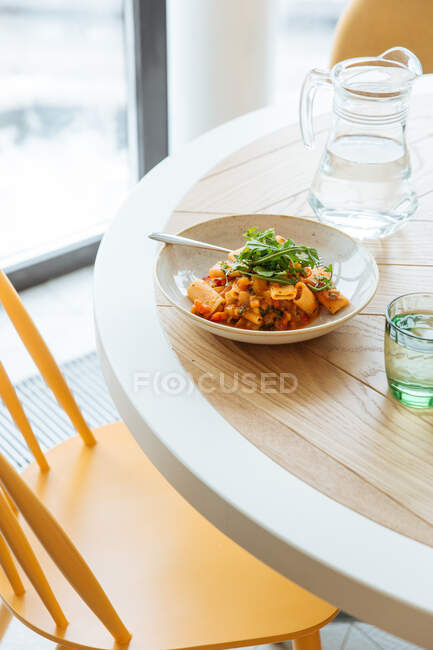 From above of tasty colorful ragout with noodle in white bowl decorated with greenery on table with glass of water — Stock Photo