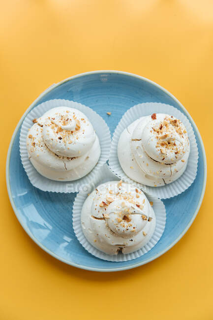 Top view of creamy meringue decorated with pieces of nuts in blue ceramic plate on yellow table — Stock Photo