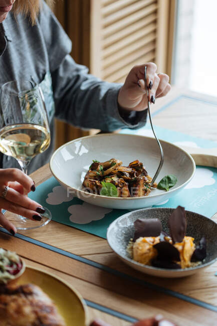 D'en haut de la culture personne manger main plat de haute cuisine sur la table avec un verre de vin withe dans un restaurant moderne — Photo de stock