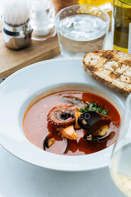Vista superior de la sopa roja de pulpo y mejillones servidos con vegetación y pan tostado en el restaurante - foto de stock