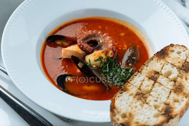 Blick von oben auf die rote Suppe aus Kraken und Miesmuscheln, serviert mit Grün und gebratenem Brot im Restaurant — Stockfoto