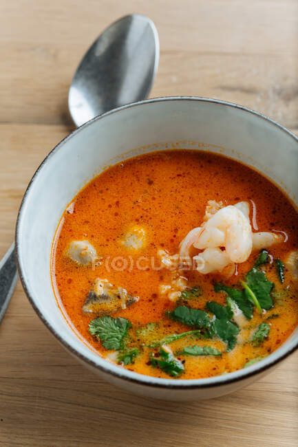 From above of spicy soup delicacy with shrimps and greenery in ceramic bowl on table with metal spoon — Stock Photo