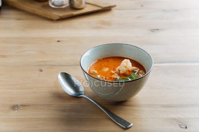 Du dessus de la délicatesse de la soupe épicée avec des crevettes et de la verdure dans un bol en céramique sur la table avec une cuillère en métal — Photo de stock