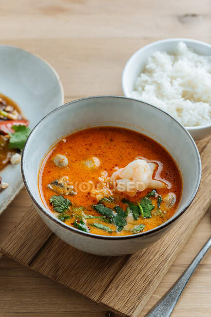 Верхний вид на красочные овощи в овальной тарелке с палочками на деревянном столе с острым супом из морепродуктов и с вареным рисом — стоковое фото