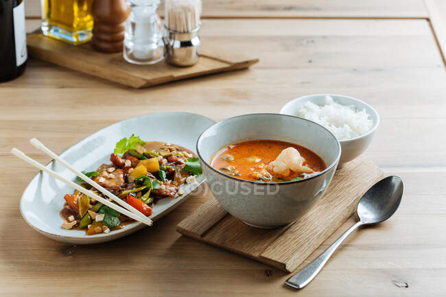 Вид зверху на барвисті овочі в овальній тарілці з паличками на дерев'яному столі з гострим супом з морепродуктів і вареним рисом — стокове фото