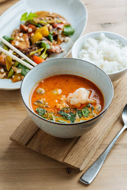Vista superior de verduras de colores en plato ovalado con palillos en mesa de madera con sopa de mariscos picantes y con de arroz hervido - foto de stock