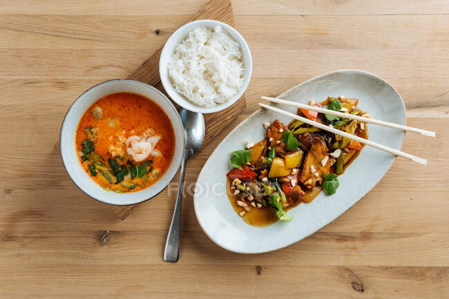 Draufsicht auf buntes Gemüse in ovalen Teller mit Essstäbchen auf Holztisch mit würzigen Meeresfrüchten Suppe und mit gekochtem Reis — Stockfoto