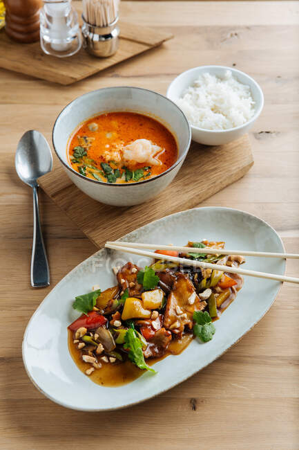 Верхний вид на красочные овощи в овальной тарелке с палочками на деревянном столе с острым супом из морепродуктов и с вареным рисом — стоковое фото