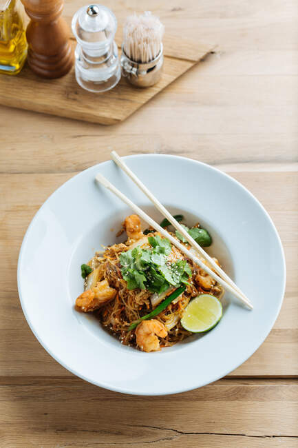 From above of tasty noodles with fried shrimps slices of lime and fresh parsley in plate with wooden chopsticks — Stock Photo