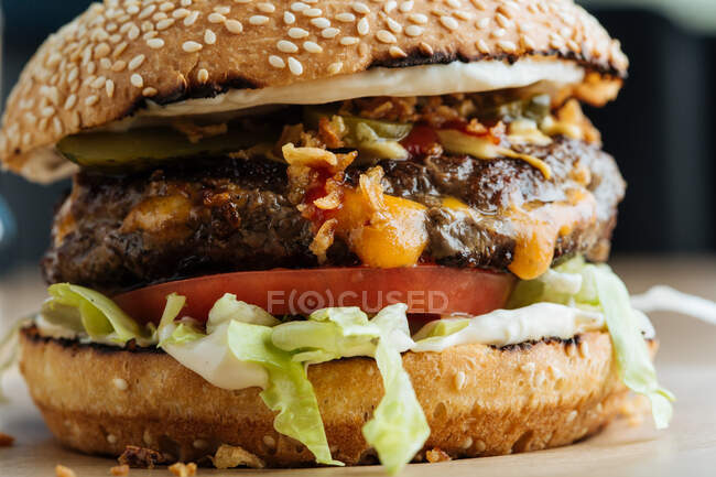 Closeup of juicy burger with tasty cutlet slices of tomatoes lettuce and cucumbers between soft roasted buns in restaurant — Stock Photo
