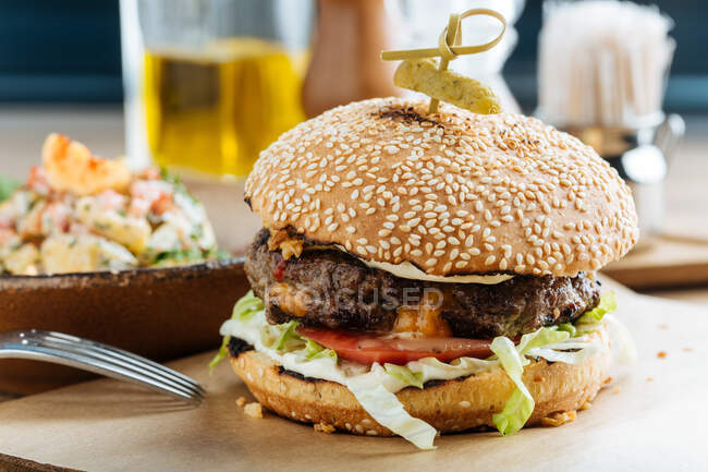 Großer Hamburger auf Papier mit Schnitzelkäse und Gemüse serviert mit Schüssel mit buntem Salat in modernem Restaurant — Stockfoto
