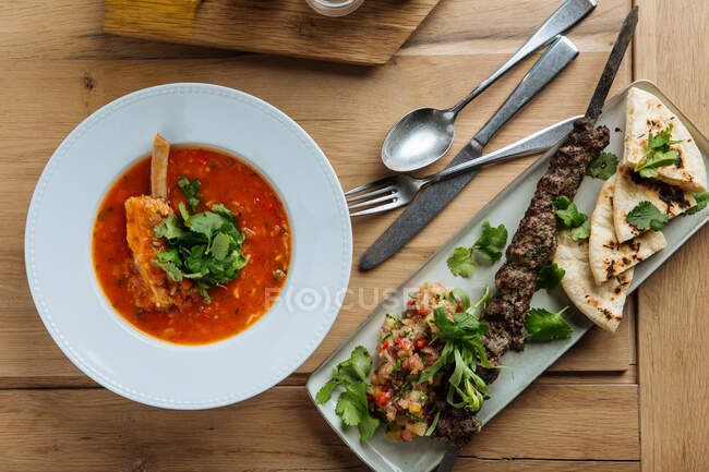 Top view of red soup with meat and fresh herbs on wooden table with kebab and flat bread in restaurant — Stock Photo